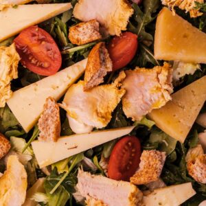 Ensalada cesar con queso semicurado, láminas de pollo, costrones, cherrys en su salsa